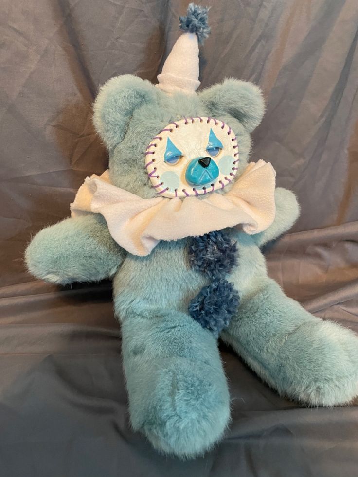 a blue teddy bear with a party hat on it's head sitting on a gray background