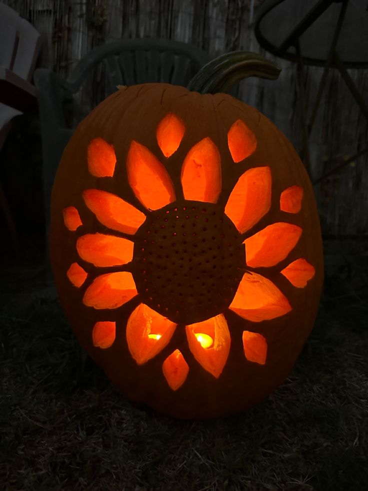 a carved pumpkin sitting on the ground with its light shining through it's petals