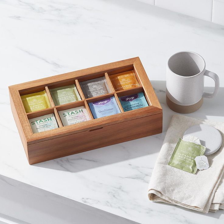 a wooden box filled with teas next to a cup and napkin on top of a counter