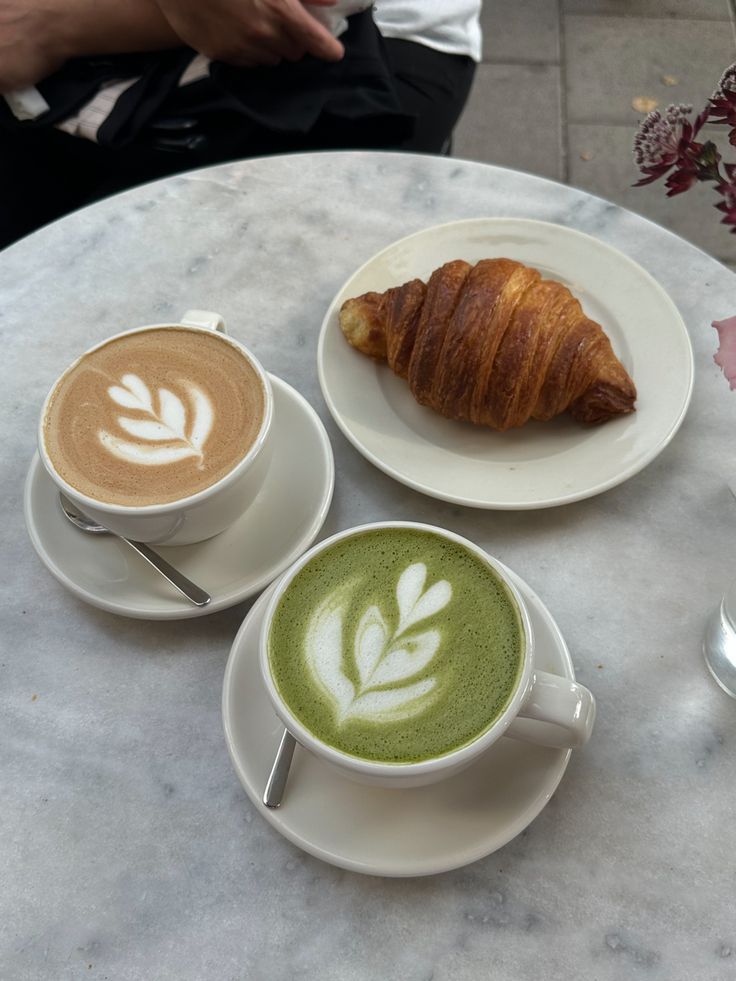 two cups of green tea, croissant and coffee on a marble table top