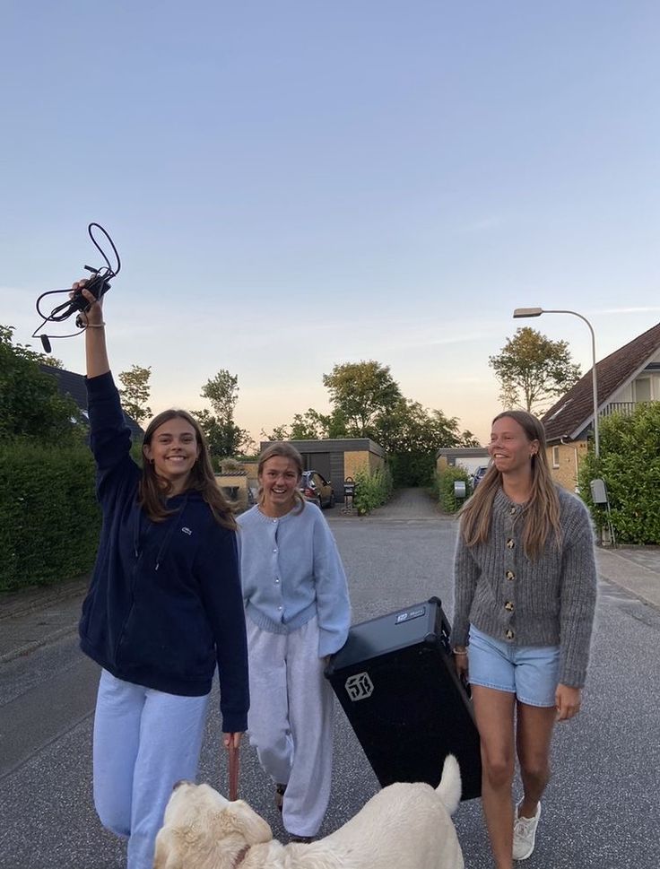 three girls are walking down the street with their dog and holding something up in the air