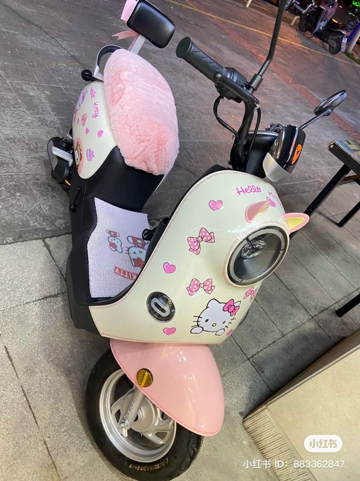 a hello kitty scooter is parked on the sidewalk with a stuffed animal in it's seat