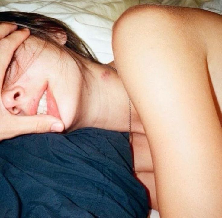 a woman laying on top of a bed with her hand under her head and eyes closed