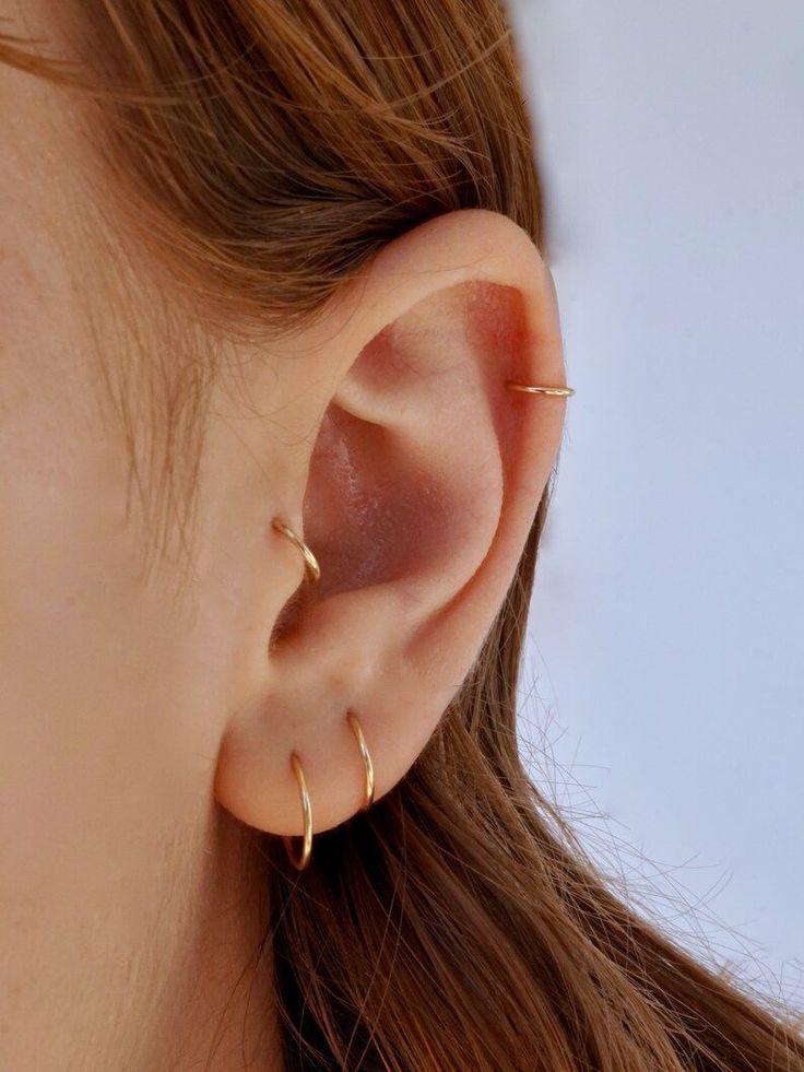 a woman's ear is shown with two small gold hoops on the side