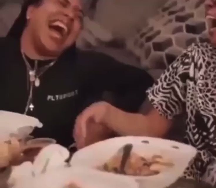 two people sitting at a table with plates of food in front of them and laughing