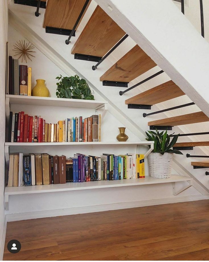 the bookshelf under the stairs is full of books and plants, along with some decorative vases