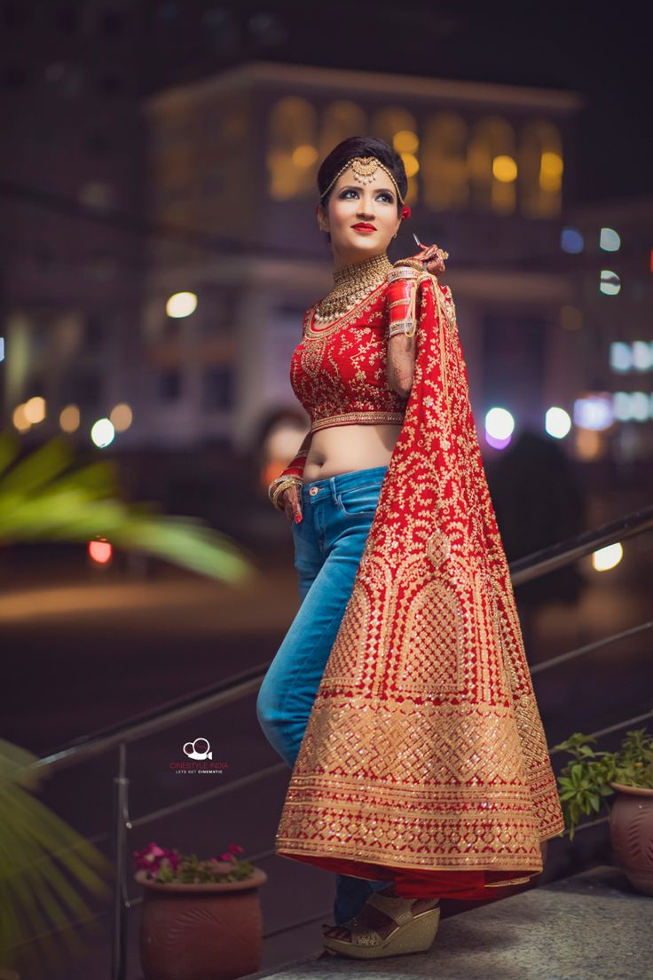 a woman in a red and gold lehenga poses for the camera at night