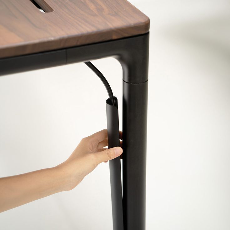 a hand is holding the handle on a wooden table with black metal frame and legs