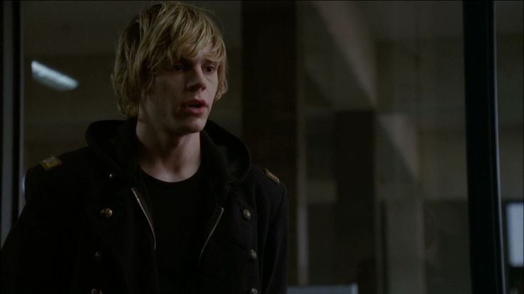 a young man standing in front of a glass door wearing a black jacket and hoodie