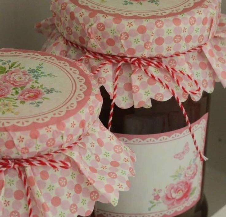 two jars with pink and white flowers on them sitting next to each other in front of a shelf