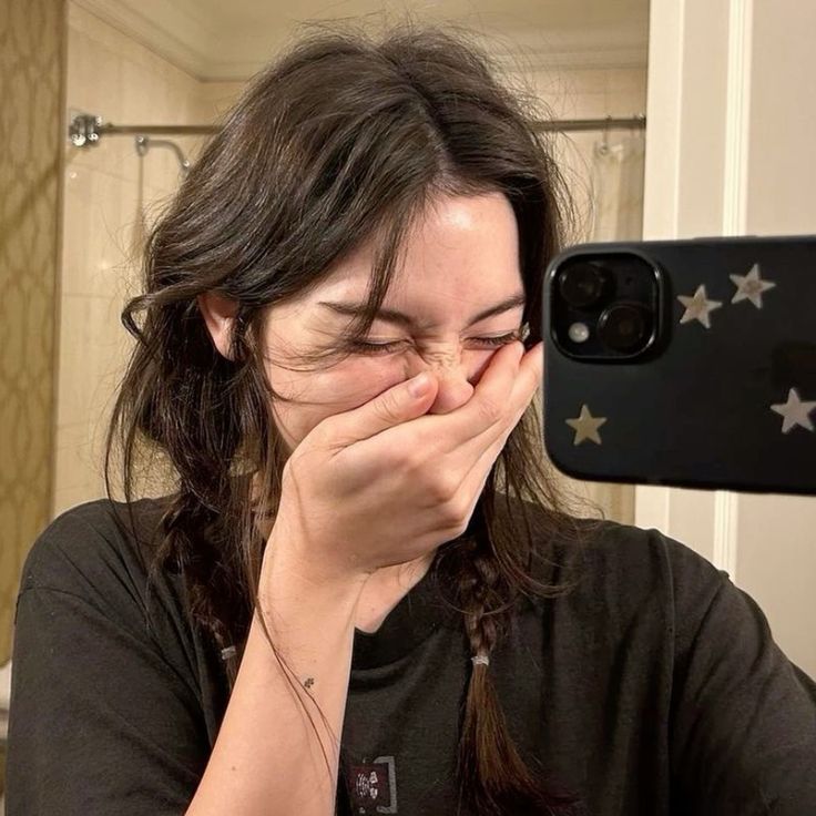 a woman covers her face with her hands while taking a selfie in the bathroom