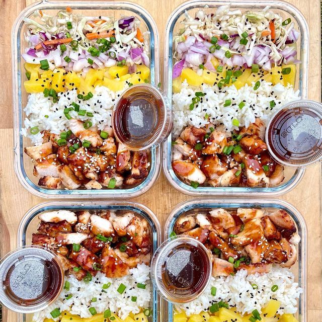 four plastic containers filled with food on top of a wooden cutting board next to rice and sauce