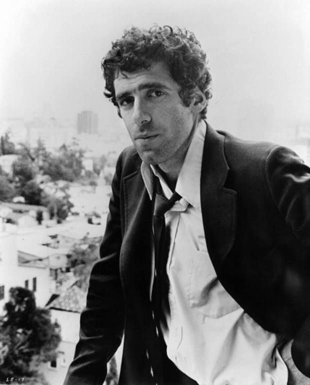 a black and white photo of a man in a suit sitting on a ledge looking at the camera