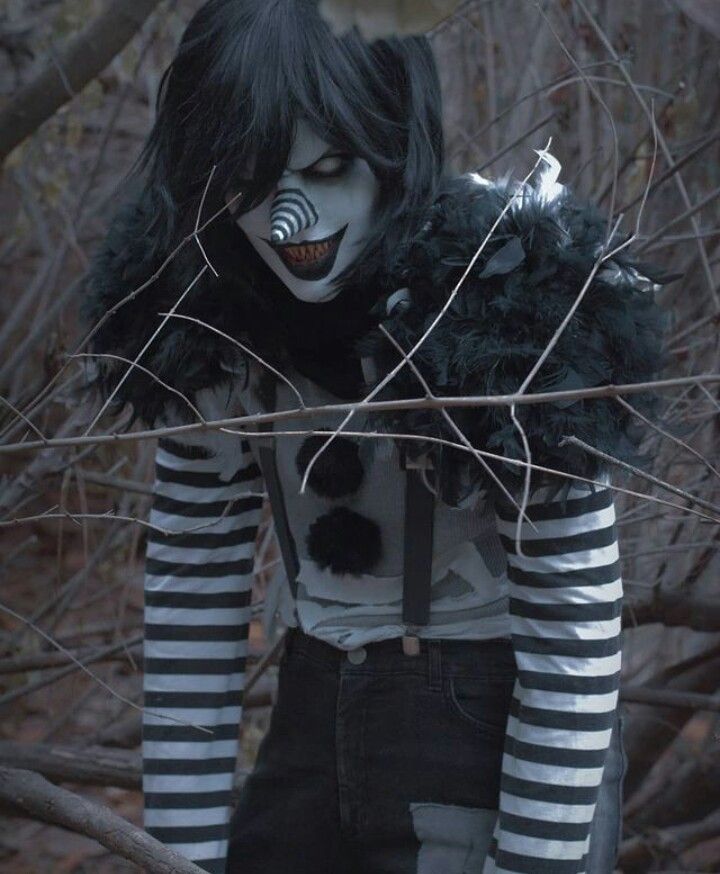 a creepy clown with black and white makeup standing in front of some bare tree branches