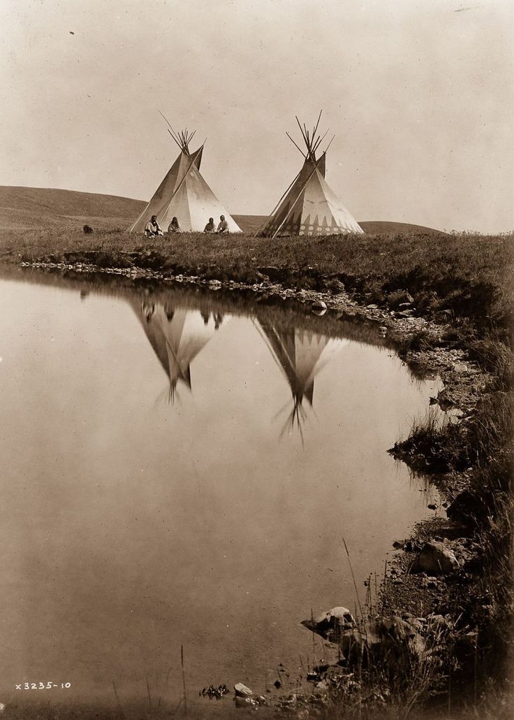 two teepees are standing next to a body of water in an old photo