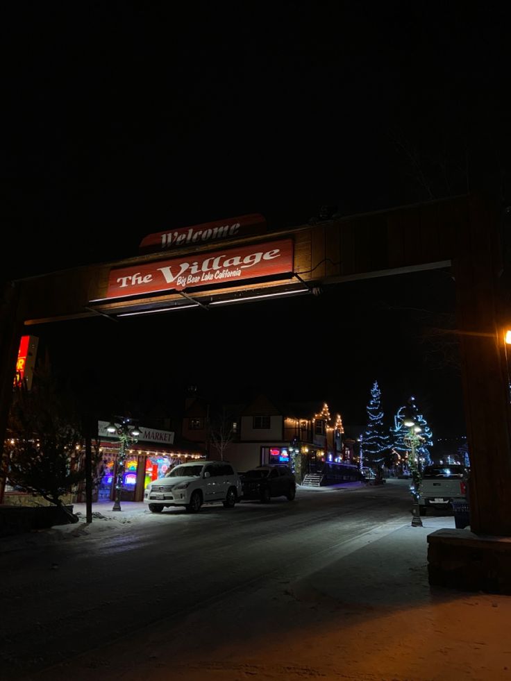 a street with cars parked in front of it and a lighted sign that says the village