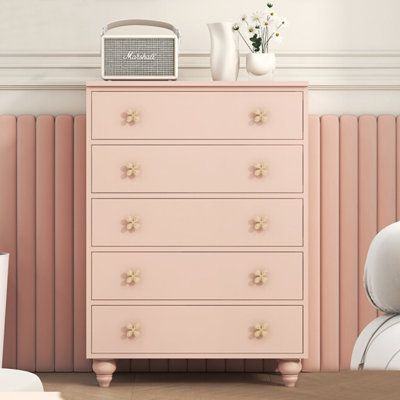 a pink chest of drawers next to a white chair and vase with flowers on top