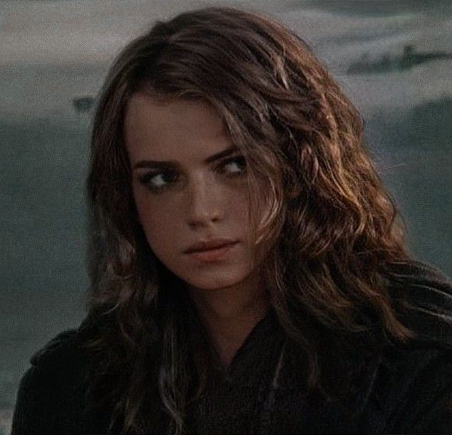 a close up of a person with long hair near the ocean and boats in the background