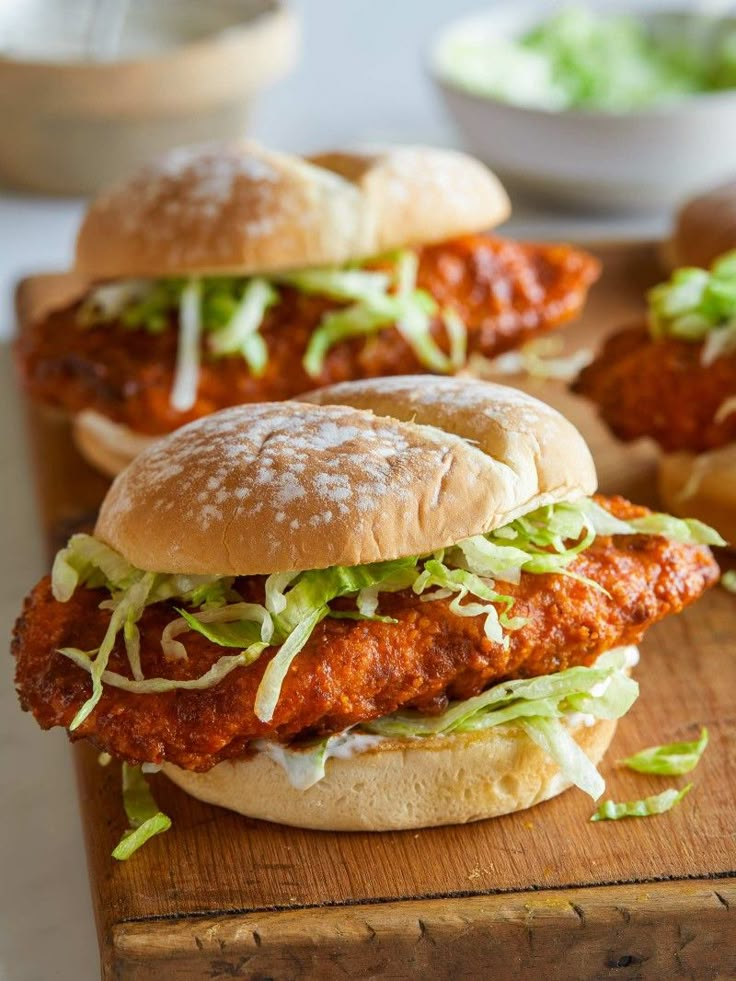 two chicken sandwiches with lettuce and tomato sauce on a wooden cutting board next to bowls of salad