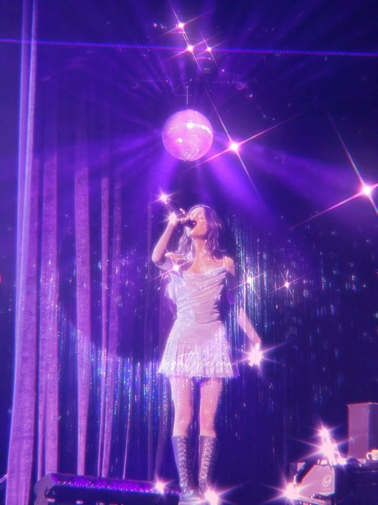 a woman in a short white dress on stage with microphone and disco balls behind her