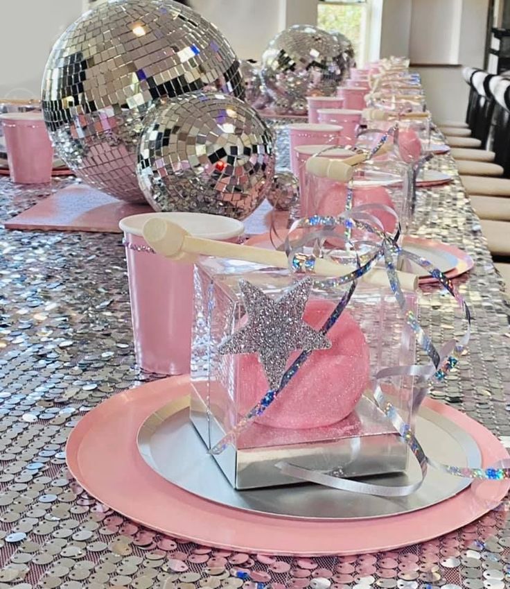 a long table with disco balls and pink plates on it, along with other decorations