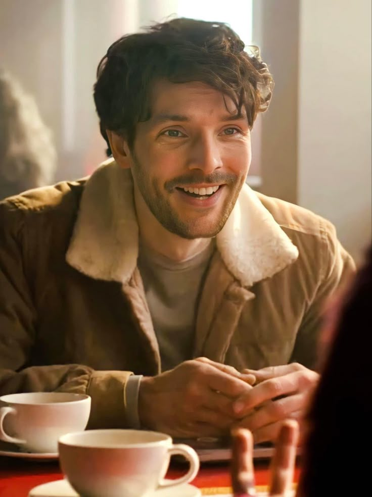 a man sitting at a table with two cups and saucers in front of him