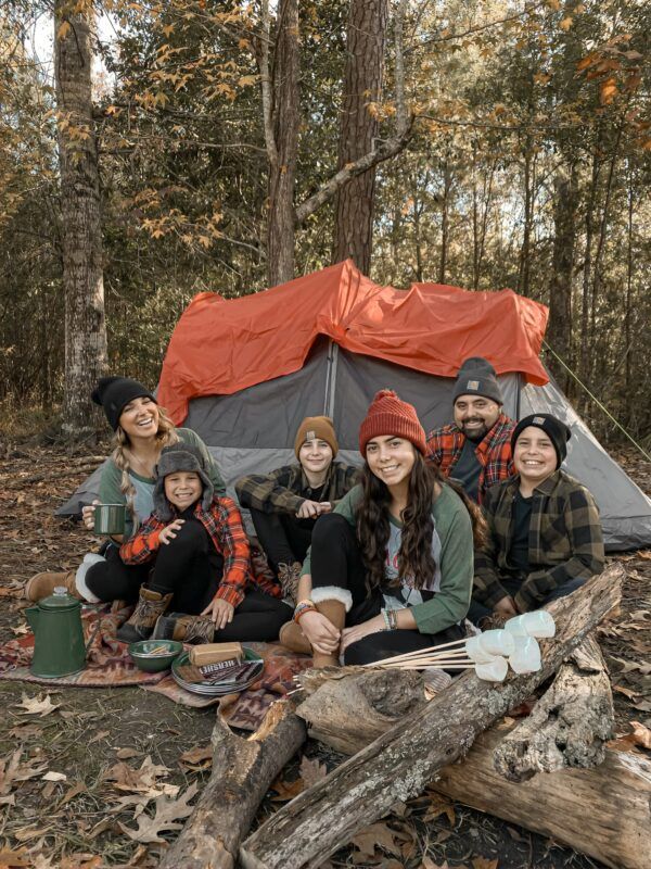 a group of people sitting around a tent in the woods