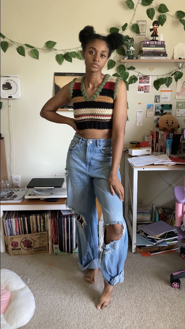 a woman wearing ripped jeans and a striped crop top standing in front of a desk