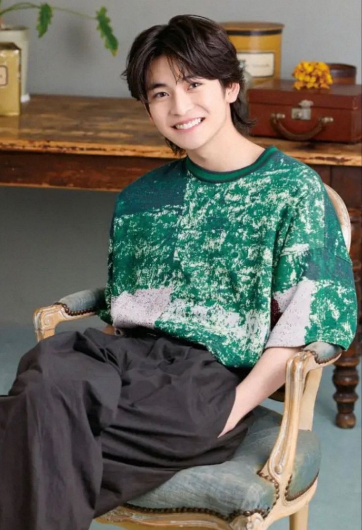 a young man sitting in a chair with his legs crossed, smiling at the camera