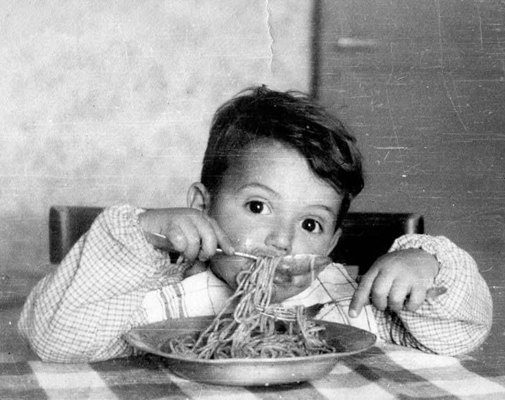 a young child eating spaghetti from a plate with the words made in italy on it