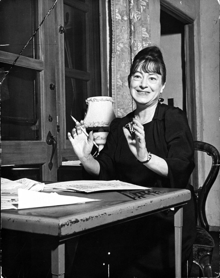 a black and white photo of a woman sitting at a table with a cup in her hands