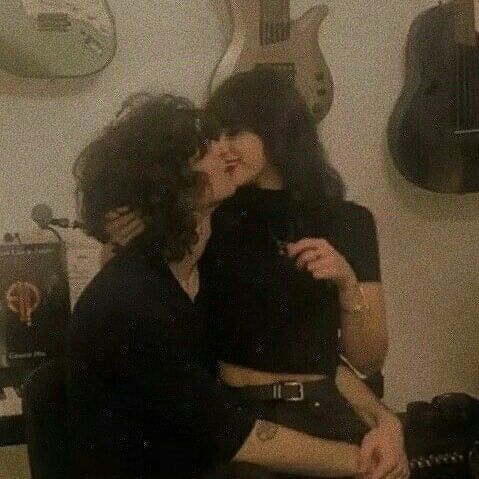 two women sitting next to each other with guitars on the wall in the back ground