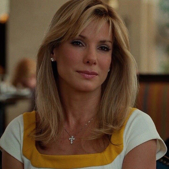 a woman with blonde hair wearing a yellow and white top sitting in front of a table