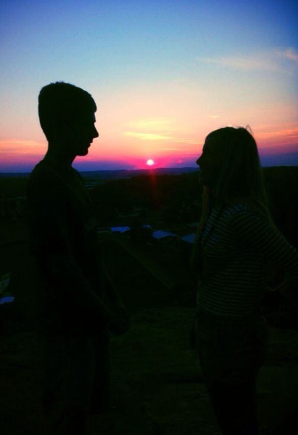 two people standing next to each other at sunset