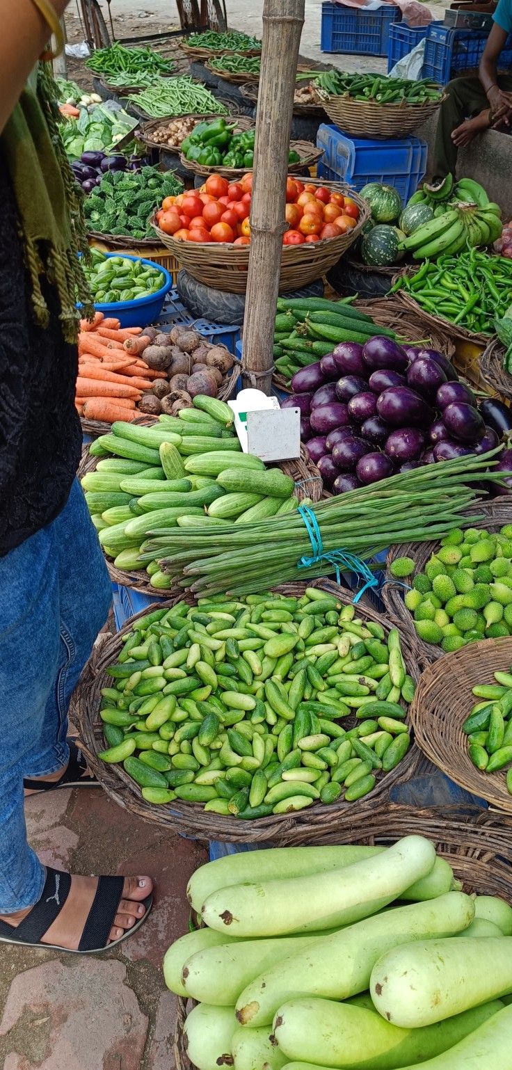 there are many different types of vegetables on display at this outdoor market stall, including bananas, eggplant, cucumbers and other fruits