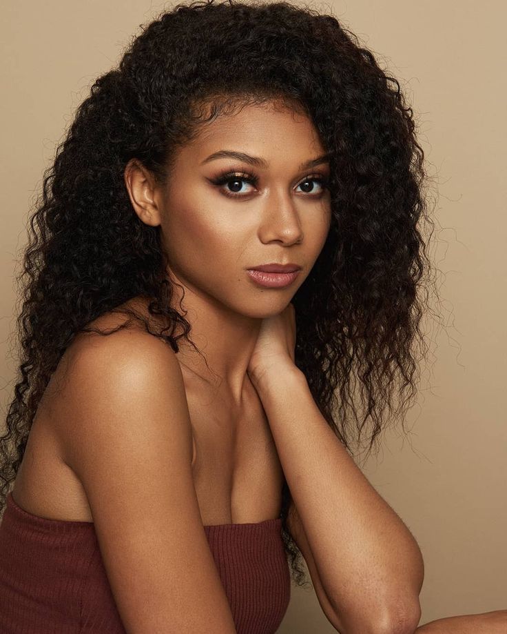 a woman with curly hair sitting on the floor wearing a brown top and looking at the camera