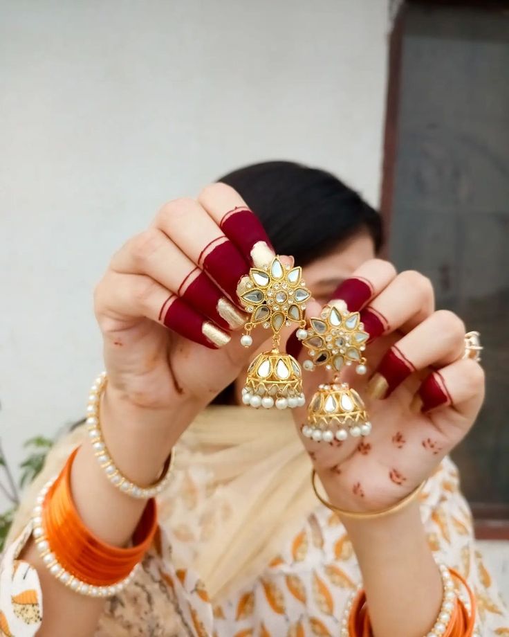 a woman holding up two pairs of jewelry