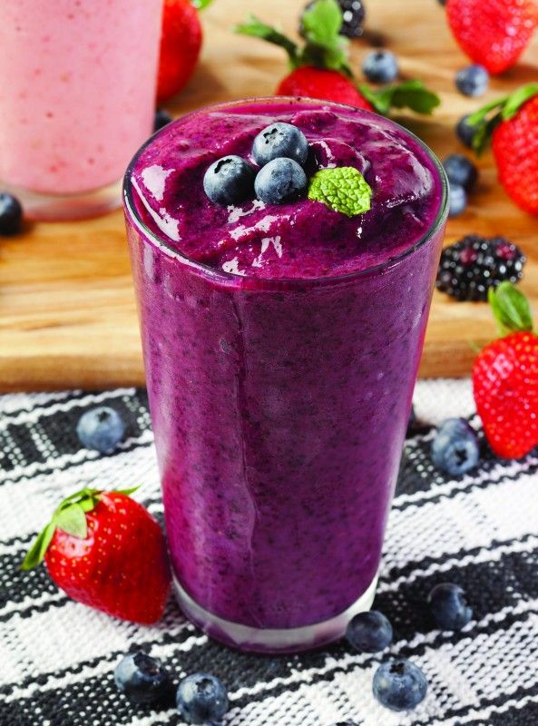 two smoothies with blueberries and strawberries on a table next to other fruit