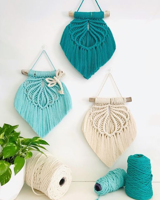 three macrame wall hangings with yarn and potted plant next to them