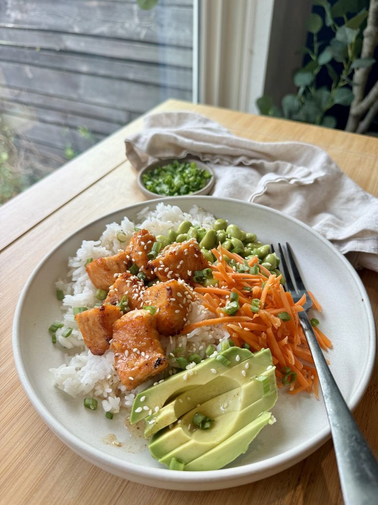 a white plate topped with rice, avocado and salmon next to a fork