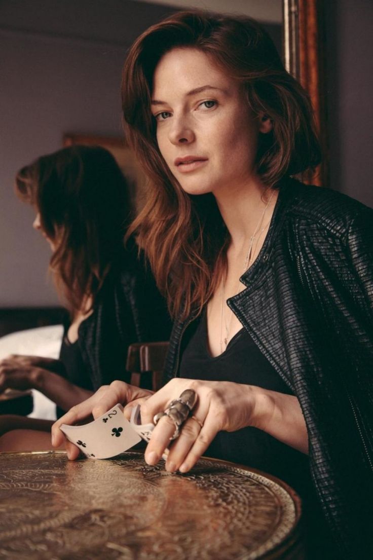 a woman sitting at a table with a card in her hand and playing cards on the table