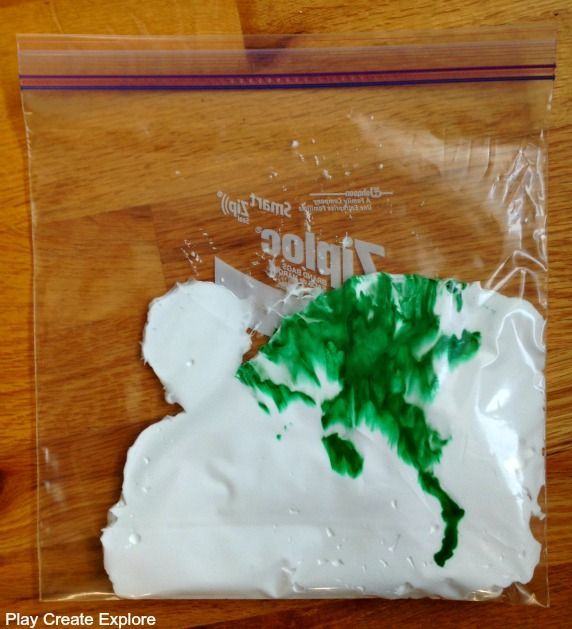 a plastic bag filled with white frosting and green leafy trees on top of a wooden table