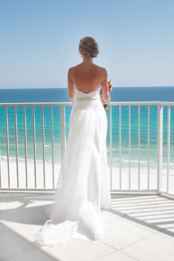 a woman in a white wedding dress looking out at the ocean from a balcony area