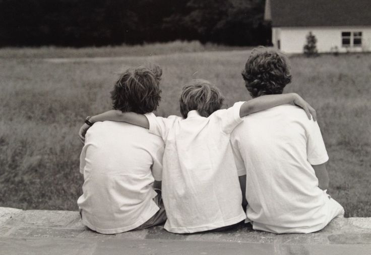 three young boys sitting on the edge of a stone wall in front of a field