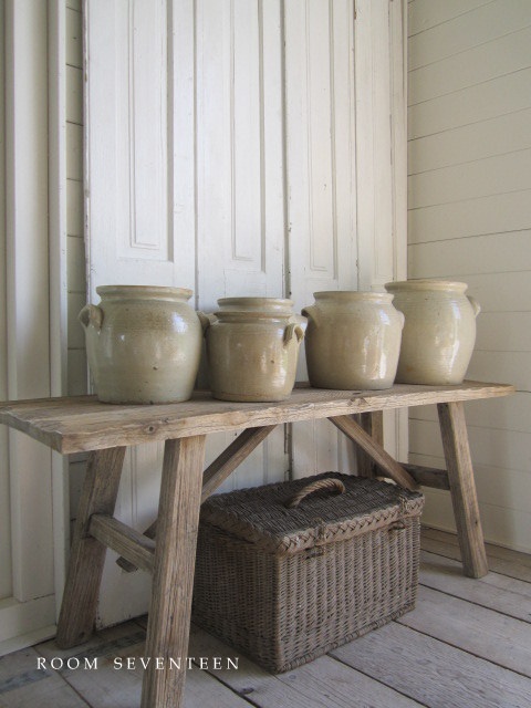 some white jars are sitting on a wooden table next to a wicker basket and an old door