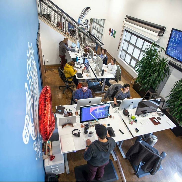 people working at desks in an office with computers on the desk and large windows