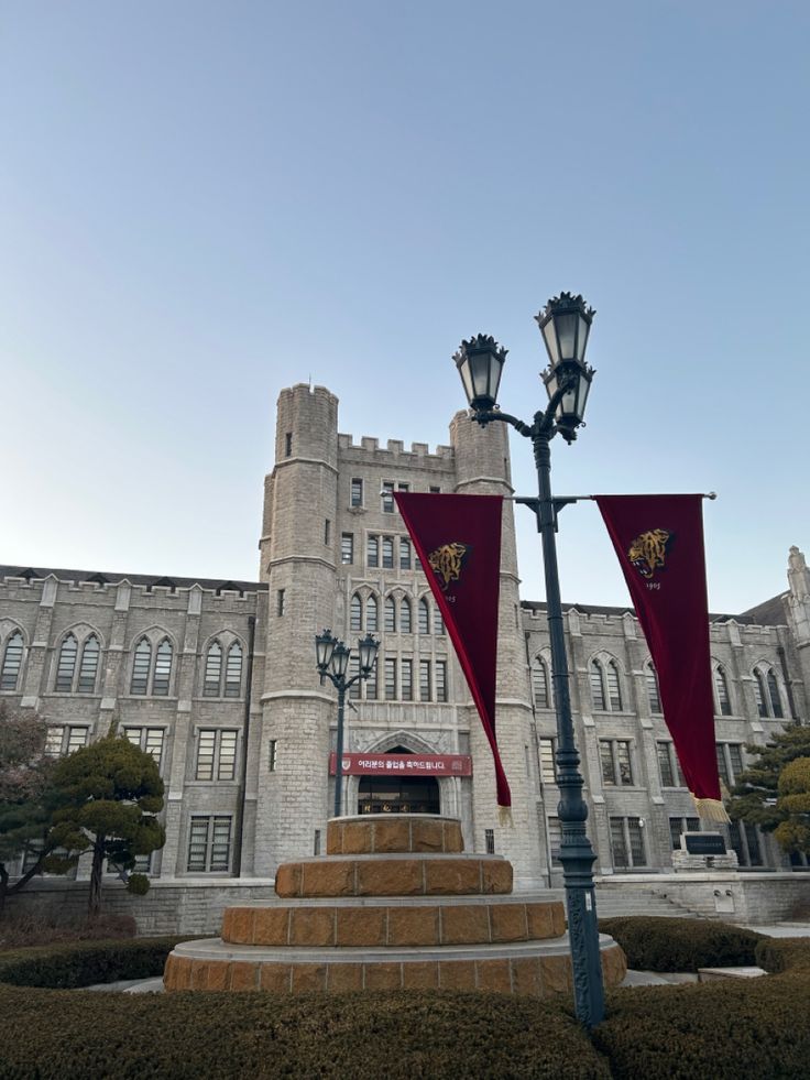 two red flags are hanging from a lamp post in front of a large castle like building