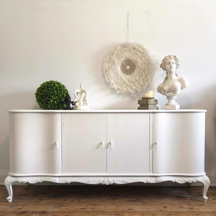 a white dresser sitting on top of a hard wood floor next to a vase and potted plant