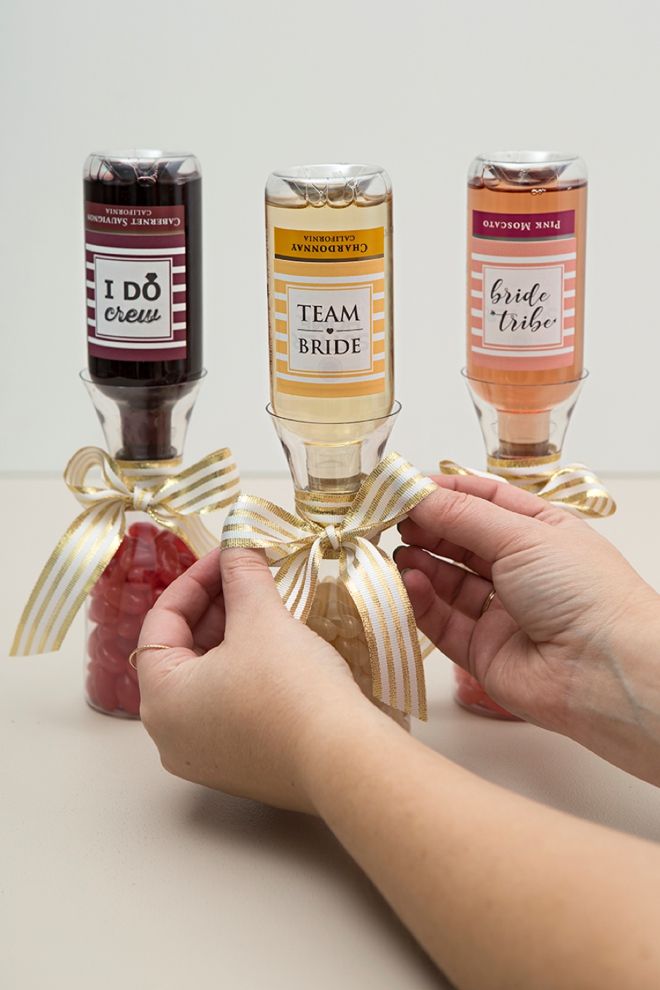 three bottles of wine tied to ribbons with hands holding grapes and raspberries in front of them