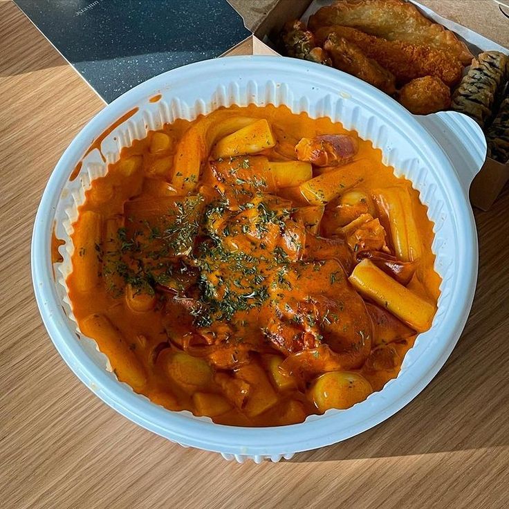 a white bowl filled with food next to a box of chicken wings and some bread